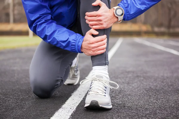 Plan recadré d'un jeune coureur tenant sa jambe dans la douleur . — Photo