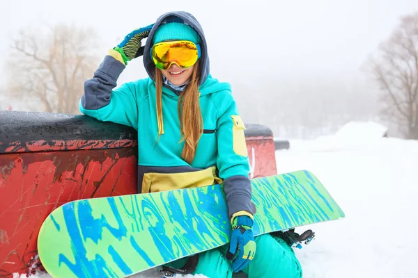 Beautiful happy young snowboarder sitting with her snowboard. — Stock Photo, Image