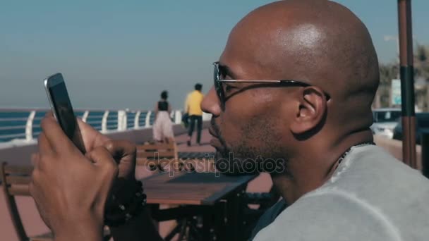 Чоловік зі смартфоном на вулиці біля моря — стокове відео