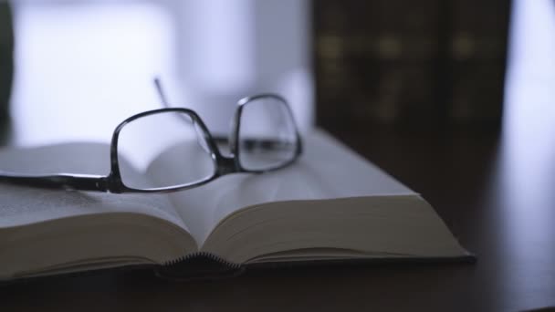 Altes Buch auf dem Schreibtisch mit moderner Brille — Stockvideo