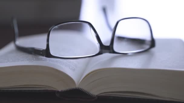 Altes Buch auf dem Schreibtisch mit moderner Brille — Stockvideo