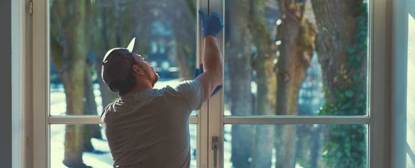 Joven está usando un trapo y una escobilla mientras limpia ventanas . — Foto de Stock