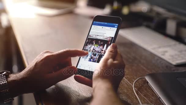 Молодой человек пользуется приложением Facebook на яблочном iPhone 6s plus в офисе — стоковое видео