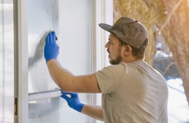 genç adam bir bez ve çekçek windows, profesyonel pencere temizleyici temizlerken kullanıyor.