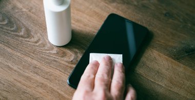 Temiz akıllı telefon için dezenfekte mendilleri olan cep telefonu ekranını temizleyen kişi. COVID-19 Coronavirüs Salgın Önleme Konsepti.