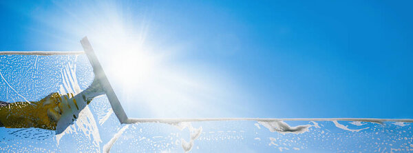 Window cleaner cleaning window with squeegee and wiper on a sunny day with a bright blue sky.