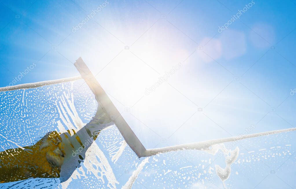Window cleaner cleaning window with squeegee and wiper on a sunny day with a bright blue sky.