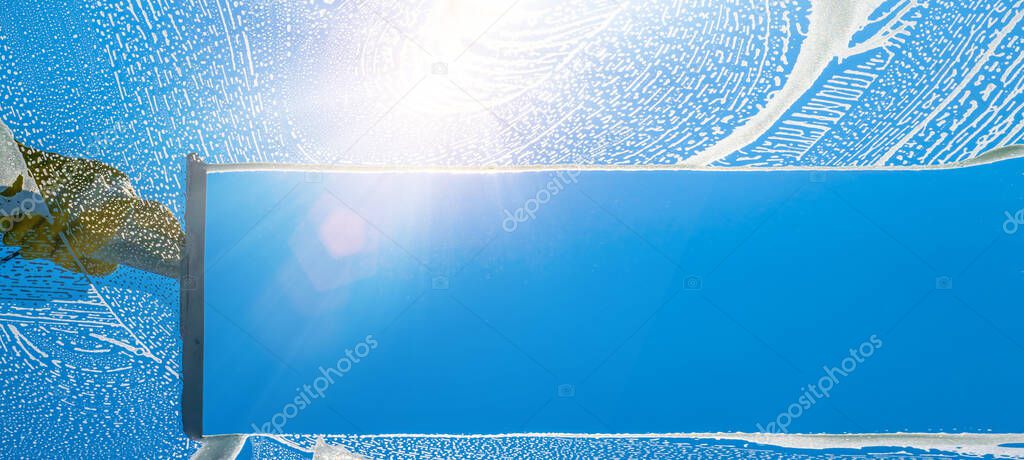 Window cleaner cleaning window with squeegee and wiper on a sunny day with a bright blue sky.