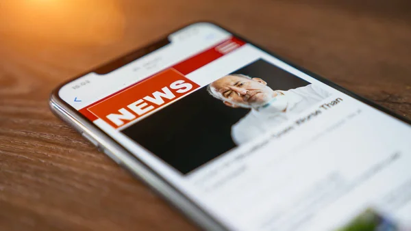 Online news on a smart phone. Close up of businessman reading news or articles in a mobile phone screen app. Hand holding smart device. Mockup website. Newspaper and portal on internet. Displayed news are not reality related
