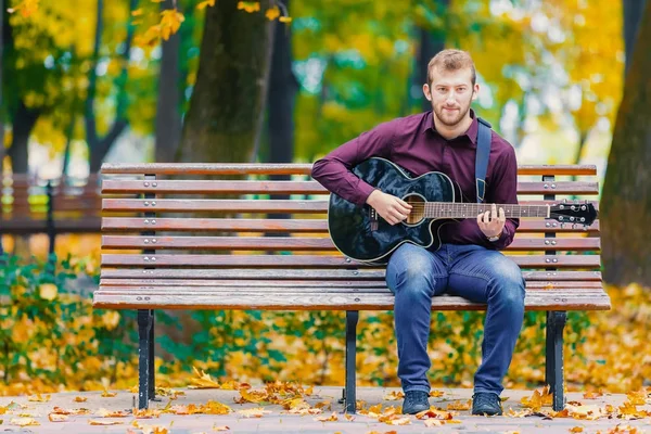 Joven con guitarra sentado en el banco — Foto de Stock