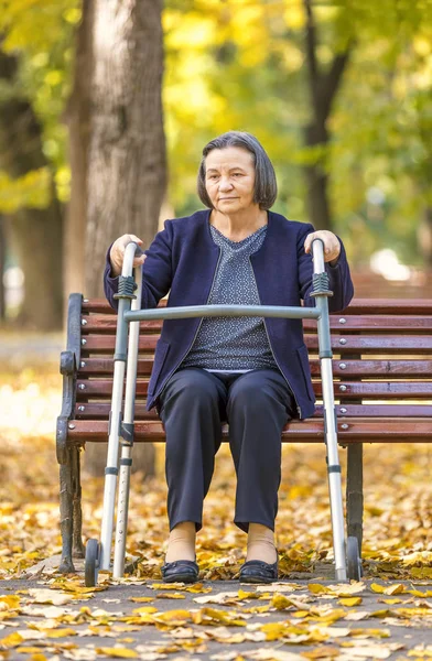Senior vrouw met walker zittend op bankje buiten — Stockfoto