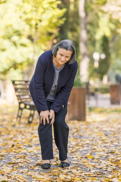 Senior woman having knee pain walking in park — Stock Photo, Image
