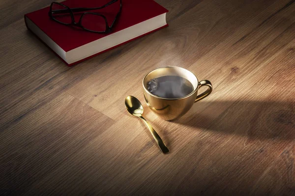 Libro y anteojos cerca de la taza de café dorado Imagen de archivo