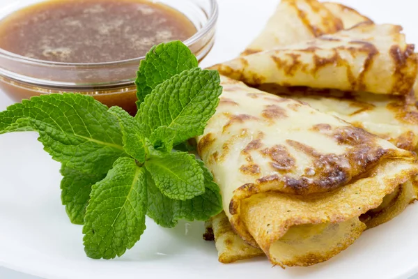 Crepes en un plato blanco con hojas de menta y una taza de miel —  Fotos de Stock