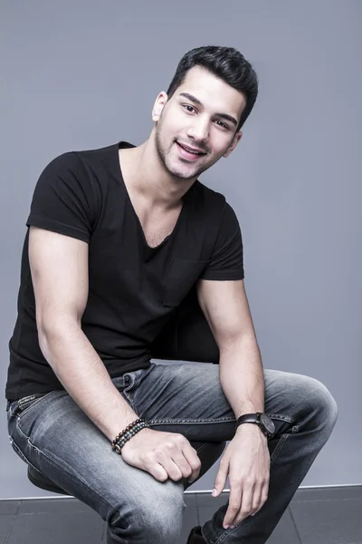 Young and handsome middle eastern man in black t-shirt on grey background, studio portrait