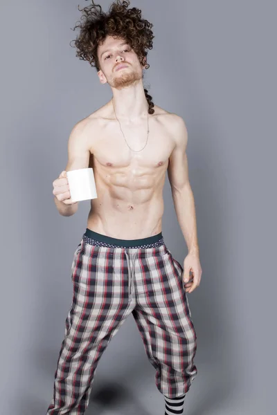 Attractive young man with long ginger curly hair having a cup of coffee or tea, studio portrait