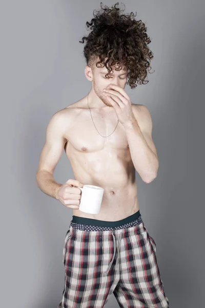 コーヒーや紅茶 スタジオ ポートレートの杯を持つ長い巻き毛を持つ魅力的な若い男 — ストック写真