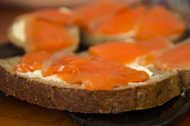 Taze somonlu sandviç, tuzlu somon balığı, tereyağı ve siyah tabakta siyah ekmek.