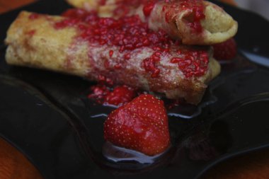 Süzme peynir ve çilek reçeli ile doldurulmuş krep ve siyah tabakta böğürtlen.