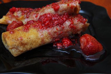 Süzme peynir ve çilek reçeli ile doldurulmuş krep ve siyah tabakta böğürtlen.