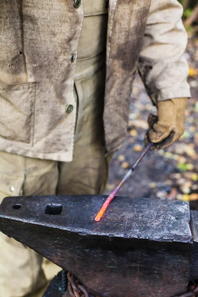 Blacksmith holds hot steel rod on anvil — Stock Photo, Image