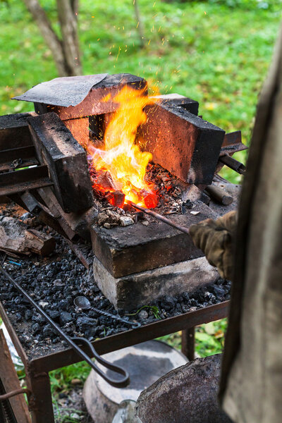 Blacksmith heats steel rod in forging furnace
