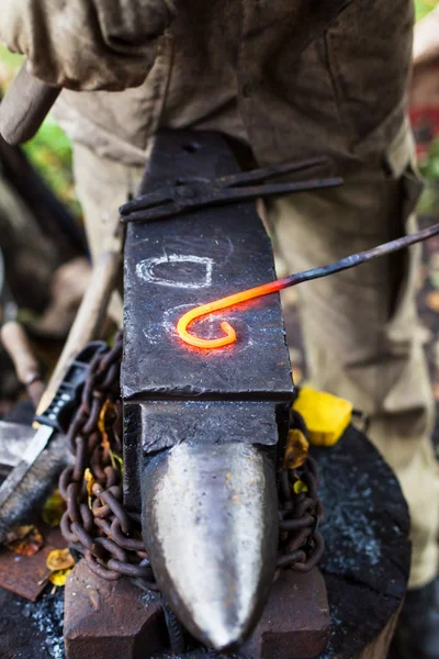 Blacksmith curves iron buckle with hammer on anvil — Stock Photo, Image