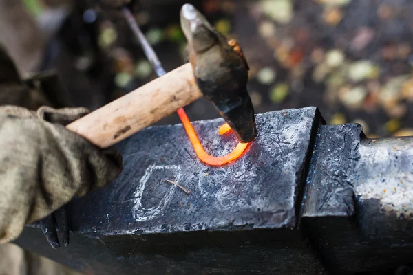 Blacksmith forges iron buckle with hammer on anvil — Stock Photo, Image