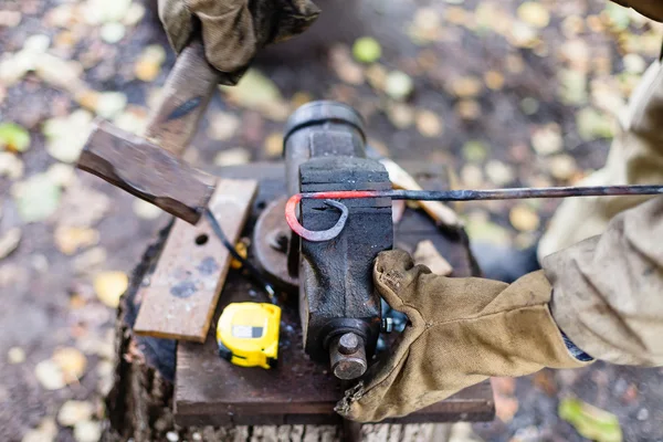 Smeden smider heta röda järnspett i skruvstäd — Stockfoto