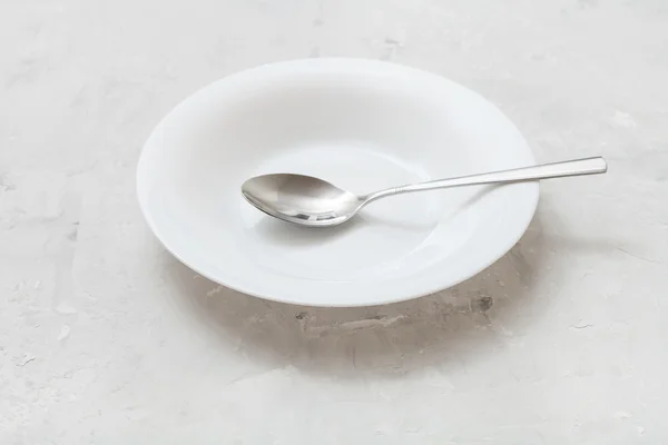 White deep plate with steel spoon on gray concrete — Φωτογραφία Αρχείου