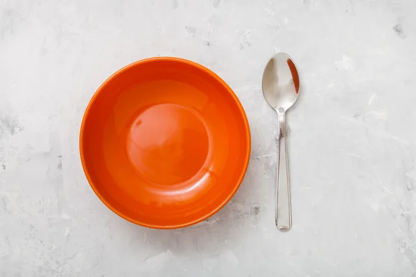 Top view orange bowl and spoon on concrete plate — Stock Photo, Image