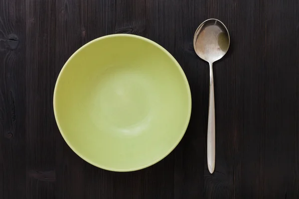 Top view green bowl and spoon on dark brown table — Stock Photo, Image