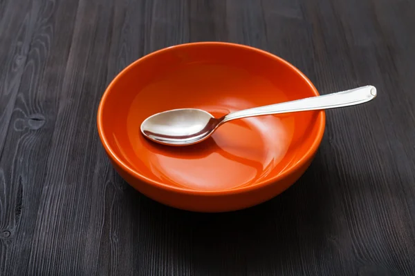 Orange bowl with spoon on dark brown board — Stockfoto