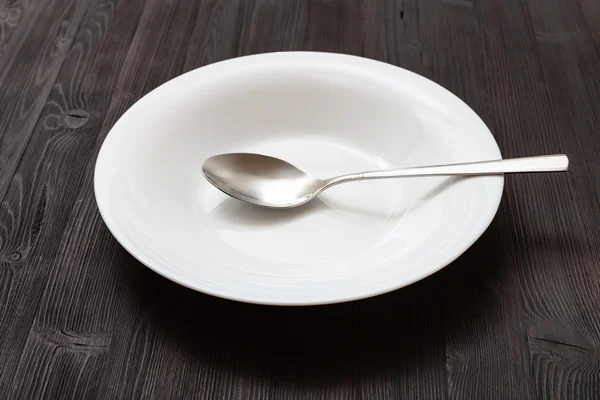 Fehér mély tányér kanállal, sötét barna asztal — Stock Fotó