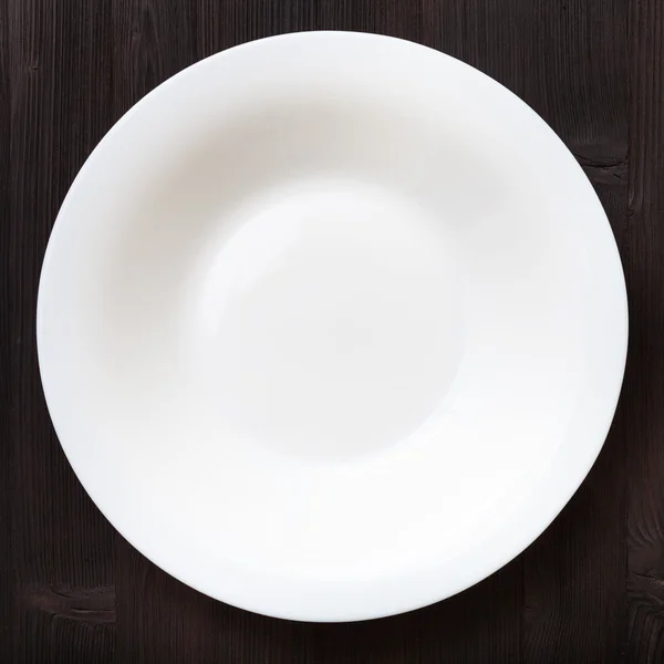 Above view of white deep plate on dark brown table — Φωτογραφία Αρχείου