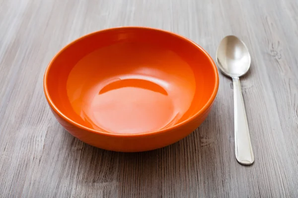 Cuenco naranja con cuchara de acero sobre mesa marrón gris —  Fotos de Stock