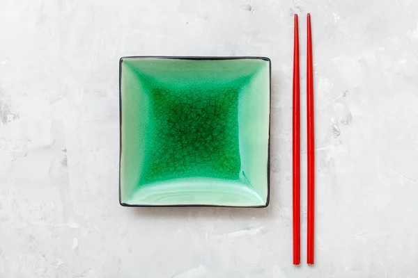 Зеленая тарелка и палочки для еды на бетоне — стоковое фото