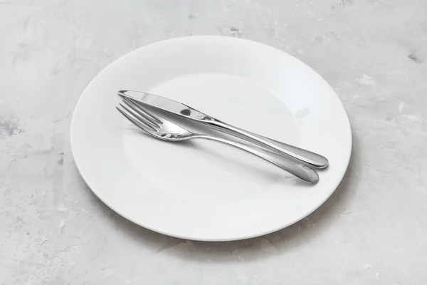 White plate with parallel knife, spoon on concrete — Stock Photo, Image