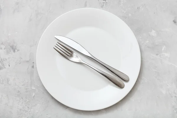 Top view of white plate with flatware on concrete — Stock Photo, Image