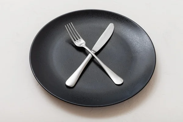 Black plate with crossing knife, spoon on white — Stockfoto