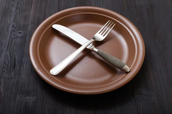 Brown plate with crossing knife, spoon on dark — Stockfoto