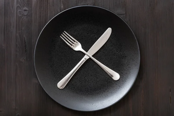 Top view black plate with flatware on dark brown — Stock Photo, Image