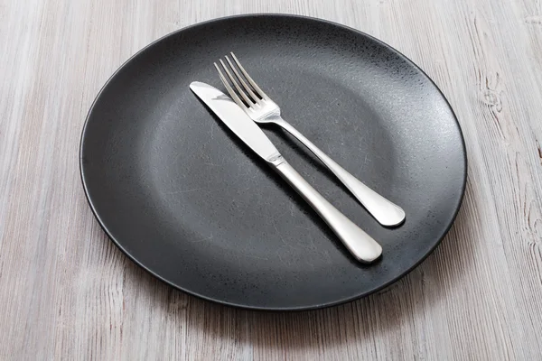 Black plate with parallel knife, spoon on gray — Stock Photo, Image