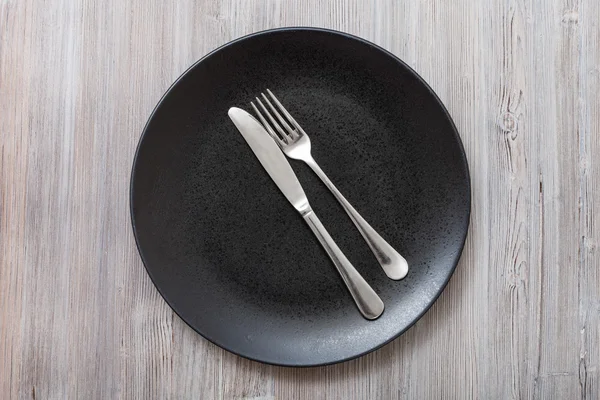 Top view of black plate with cutlery on gray — Stock Photo, Image