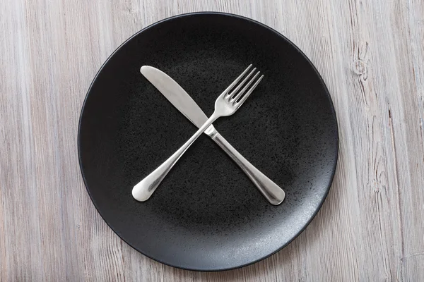 Top view of black plate with flatware on gray — Stockfoto