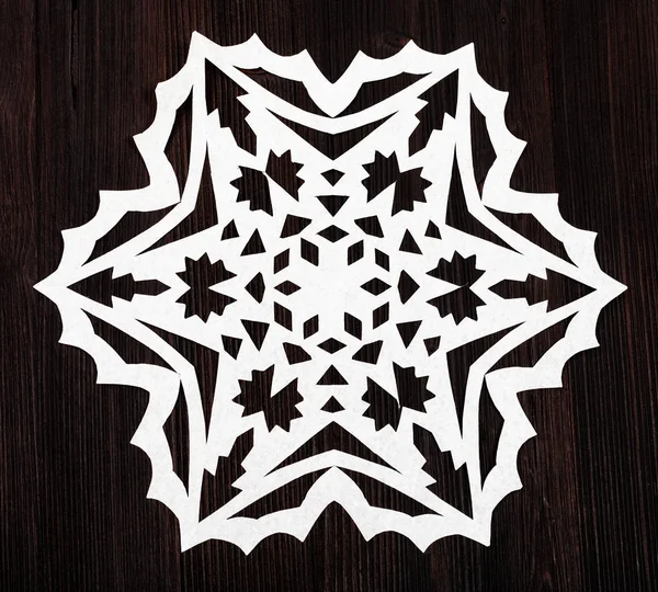 Snowflake cut out of paper on dark brown board — Stock Photo, Image