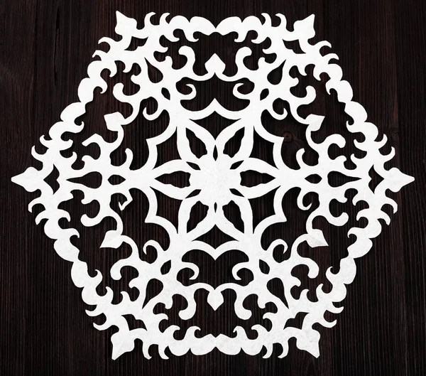 Snowflake cut out of paper on dark brown table — Stock Photo, Image