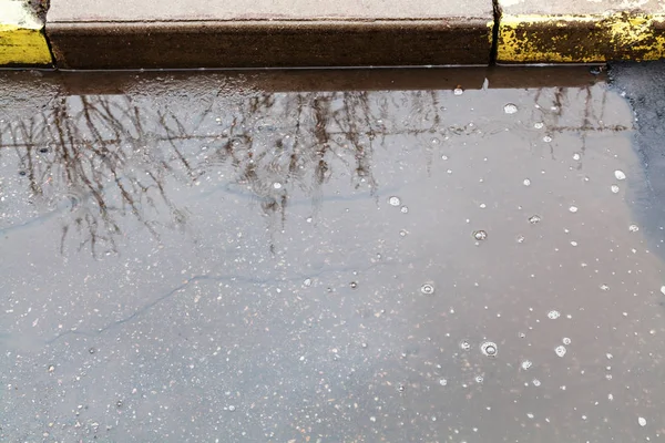 Oppervlakte van plas op stedelijke straat in regen — Stockfoto