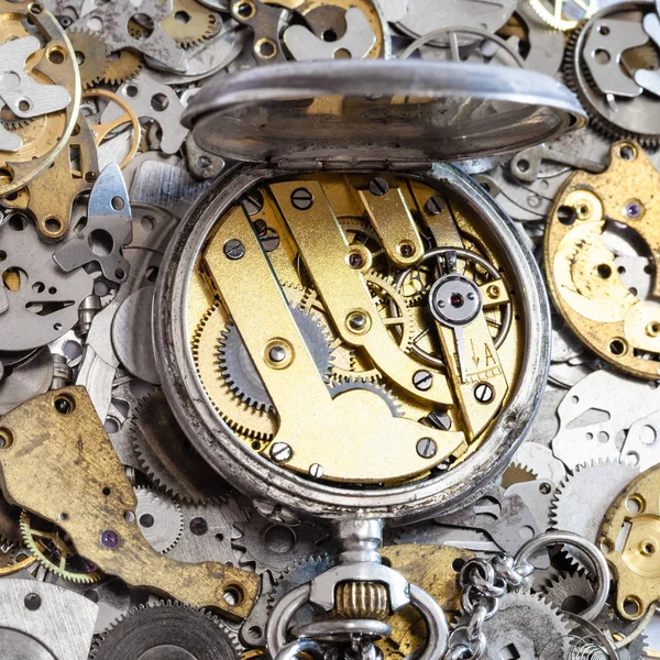 open vintage pocket watch on pile of spare parts