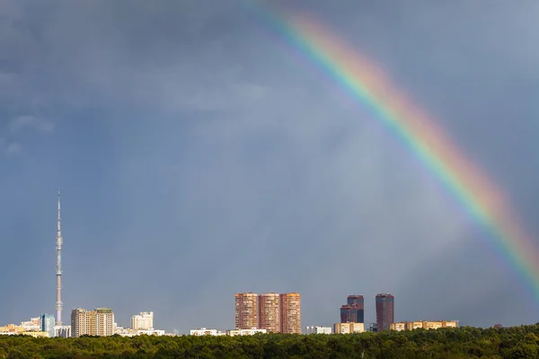 Sunbeams and rainbow in rainy sky over city — Stock Photo, Image